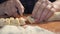 Hand of cook with knife cuts off pieces of dough on table sprinkled with flour