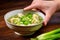 hand cradling bowl of wonton soup with green onions