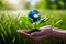 Hand cradling tree seedling, set against vibrant field backdrop and mini globe nestled in lush grass