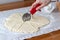 Hand cuts rolled raw curd dough with a round pizza knife into eight triangles on baking paper on a linen tablecloth