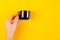 Hand with dark thermos composition on yellow background