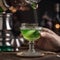 A hand delicately dropping a sugar cube into a glass of absinthe using an ornate spoon3