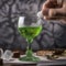 A hand delicately dropping a sugar cube into a glass of absinthe using an ornate spoon4