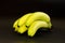 Hand of delicious, freshly washed, partly ripe green yellow bananas on a black background with waterdrops