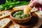 hand dipping a serving spoon into a bowl of spinach-artichoke dip for bruschetta