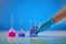 Hand in disposable glove holding beaker, purple liquid. Medical flasks, colorful chemical reagents, blue background