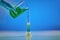 Hand in disposable glove is pouring green liquid from beaker into measuring cylinder, blue background. Coronavirus