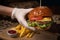 Hand in a disposable glow holding fresh craft beef burger with fried cheese, served with fresh lettuce, French fries and