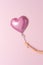 Hand of a doll with heart shaped balloon on a pink background. Love minimal concept