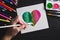 Hand drawing multi-colored heart with paints and pencils lying on black wooden table. Flat lay