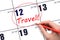 Hand drawing a red circle and writing the text TRAVEL on the calendar date 12 June. Travel planning.