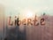 Hand drawn French word Liberte freedom in english on foggy glass on suset window