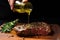 hand drizzling olive oil over a seasoned ribeye steak