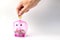 Hand drop coins on Clear pink Piggy bank on white for saving mon