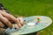 The hand of a European artist holds a mastekhin smeared in oil paint and a palette against the background of a green lawn. Blurred