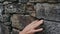 The hand exploration the stone surface of the wall, picks the stone, studies the structure of the wall.