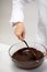 Hand of Female Confectioner mixes dark melted swiss chocolate in glass bowl