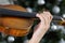 Hand of a female violinist on the fingerboard of a violin with Christmas tree