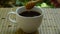 Hand filling honey from wooden scoop in black coffee cup on bamboo background