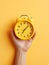 A hand firmly holds a classic clock against a vibrant yellow backdrop