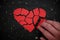 Hand fixing and repairing a broken red heart paper cutout in black background.