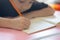 Hand focusing of adorable asian child girl is writing and reading on her paper book in the room at home with sunlight shows