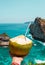 Hand with fresh coconut, ocean and cliffs tropical landscape. Vacation mood. Bali, Indonesia