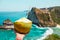 Hand with fresh coconut, ocean and cliffs tropical landscape. Vacation mood. Bali, Indonesia
