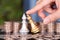 A hand in front of a large number of dollar coins helps the silver chess piece to defeat the golden chess piece