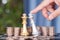 A hand in front of a large number of dollar coins helps the silver king chess piece to defeat the golden king chess piece