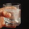 Hand with a glass of water and soluble pill on dark background.