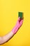 Hand with glove hoding scourer on yellow background