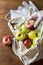 Hand in glove holds apple. Eco mesh bag with food supplies on a wooden background. Food delivery in eco-friendly packaging, zero