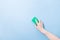 hand without a glove holds a green sponge for washing dishes and cleaning, blue background copy space, cleaning concept