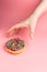 Hand grabbing chocolate frosted donut with sprinkles on pink background. Playful and joyful tasty sugary comfort food.