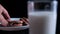 Hand grabbing cookie from a plate behind a glass of milk