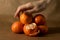 A hand grabbing from a pile of clementines on brown paper