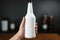 Hand grips a white labeled bottle, a minimalist design in the person\\\'s grasp