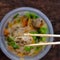 Hand hold chopsticks pick up fried spring rolls on vegan rice noodles