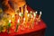 Hand hold lighter burning candlestick on red birthday cake. Anniversary party occasion with good wish and fire on the candle stick