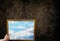 Hand hold picture frame of wide puffy cloud sky on dark grunge w