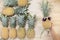 Hand hold pineapple with row of pineapple fruits on wooden table