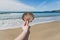 Hand holding big colorful shell in front of pristine deserted beach bokeh