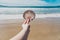 Hand holding big colorful shell in front of pristine deserted beach bokeh