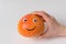 Hand holding big orange smiley on white background. Grapefruit with Googly eyes and smile