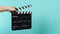 Hand is holding Black clapper board or movie clapperboard or slate on green mint or Tiffany Blue background