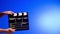 Hand is holding Black clapper board or movie slate on a blue background with a circular light. Cinema industry