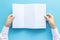 Hand holding blank white paper for letter mock up, isolated on blue background with copy space. studio shot, horizontal.