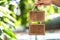 A hand holding blank wooden sign and a green bokeh background of the leaves