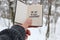 Hand holding a book with the inscription Say yes to new adventures on the background of the winter forest